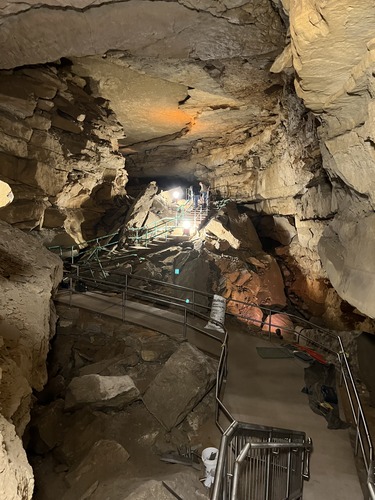 A concrete path with stairs travels over large piles of rock inside a rocky cave.