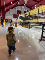 A child in a junior ranger cutout head band, behind him is a plane display. 