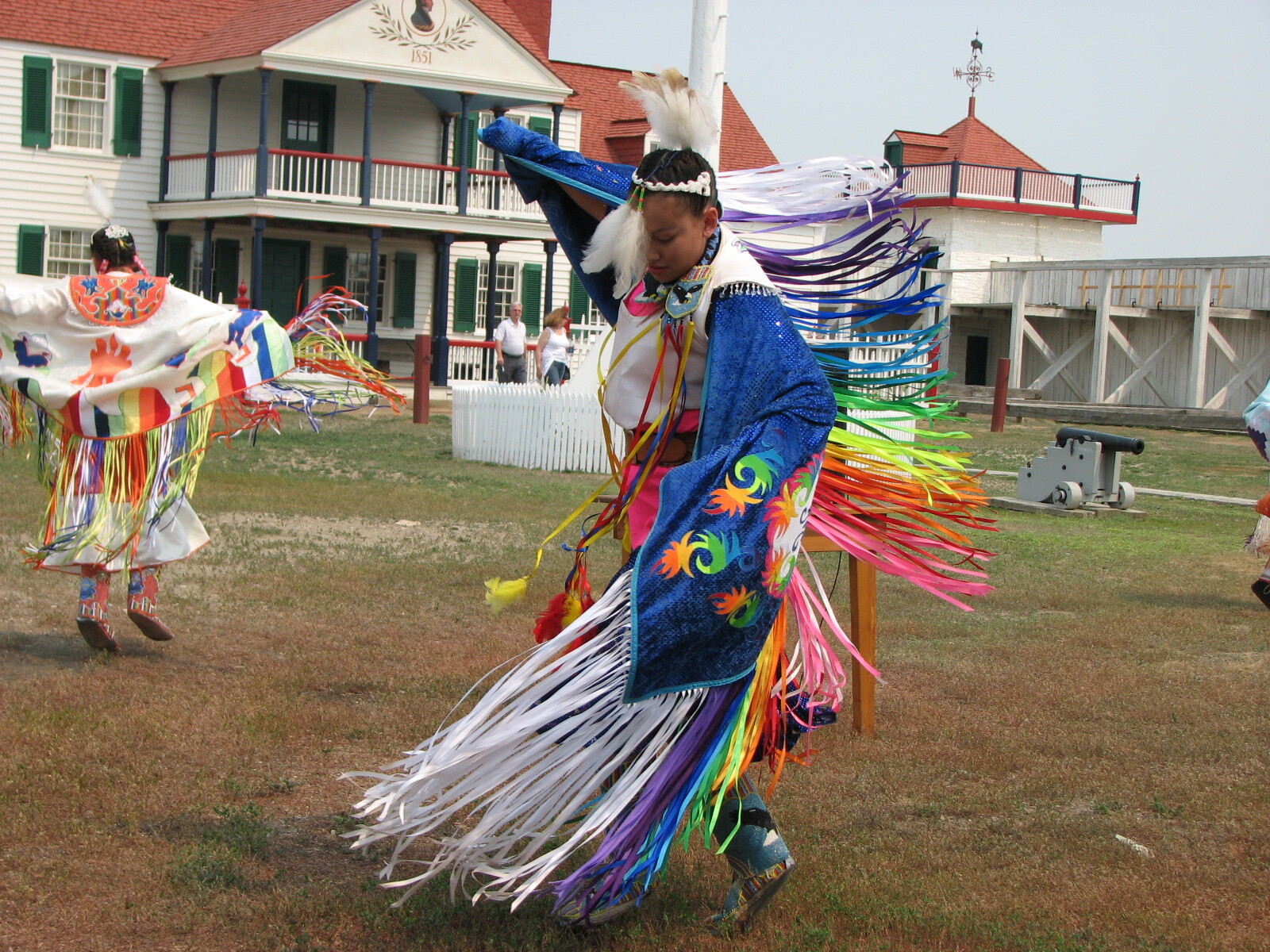 Girls in traditional American Indian dress with shalls that have long rainbow fringe dance