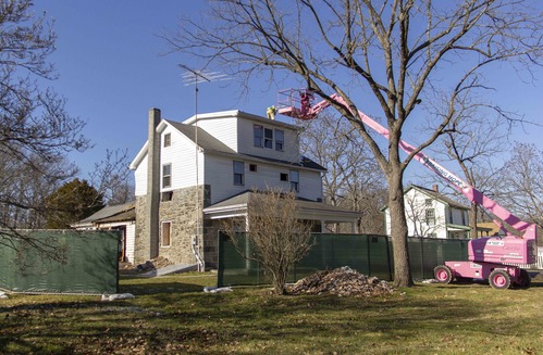 Hired contractors begin selective demolition on the exterior of the house. There is a pink construction lift off to the side, and a construction worker on the modern roof.