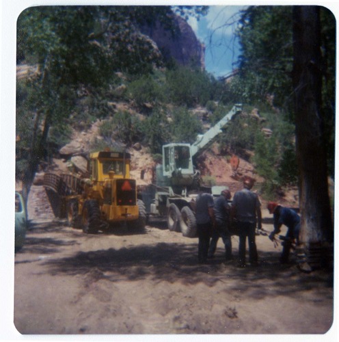 Four men securing cables for pulley system used to move new Grotto footbridge into place, crane and equipment parked nearby.