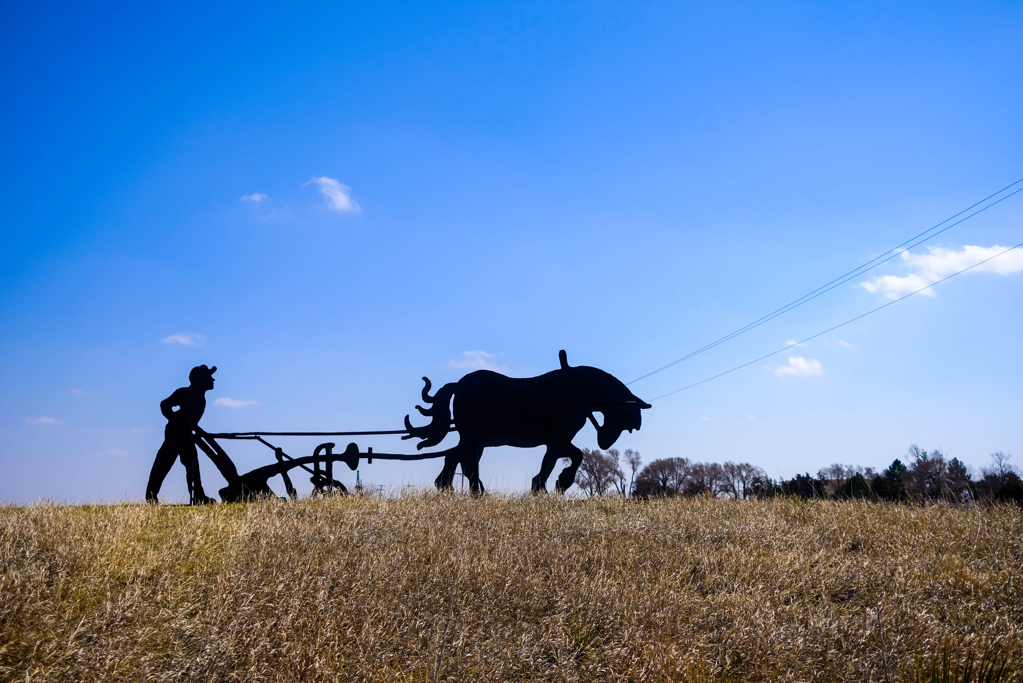 A metal silhouette of a horse and farmer with plow.