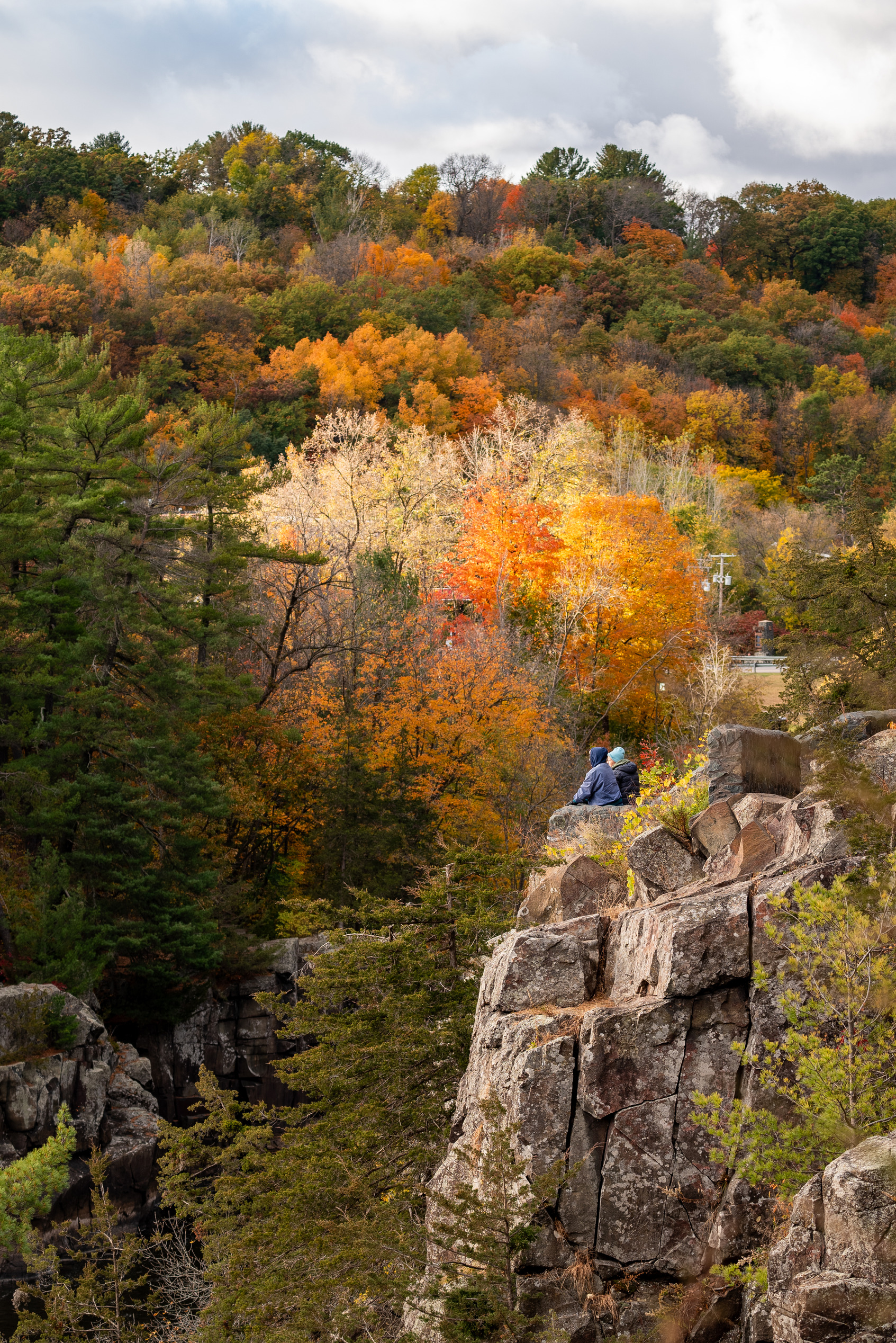 Photograph of colorful autumn landscape with two people in the distance looking out from a rocky cliffside. 