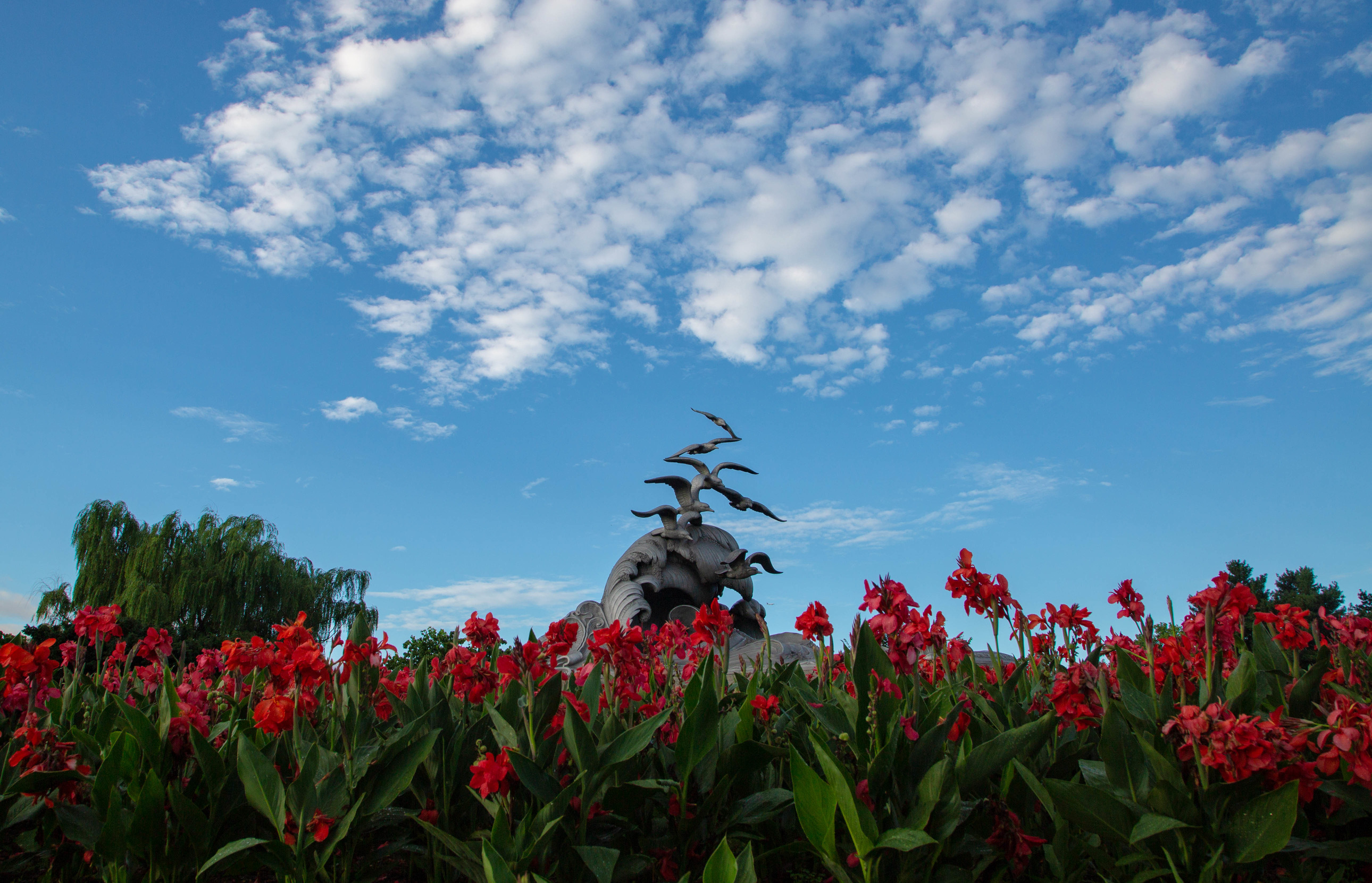Statue of waves and seagulls surrounded by red flowers