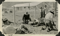 This is an historic black and white photograph from the Scotty's Castle Historic Photograph Collection, Death Valley National Park of Horse hobbled on ground to trim hooves by men. Albert M. Johnson holding a rope. Carrie Lee Johnson and Edna Devlin watching. April 23, 1928. Photographed by Mat Roy Thompson.