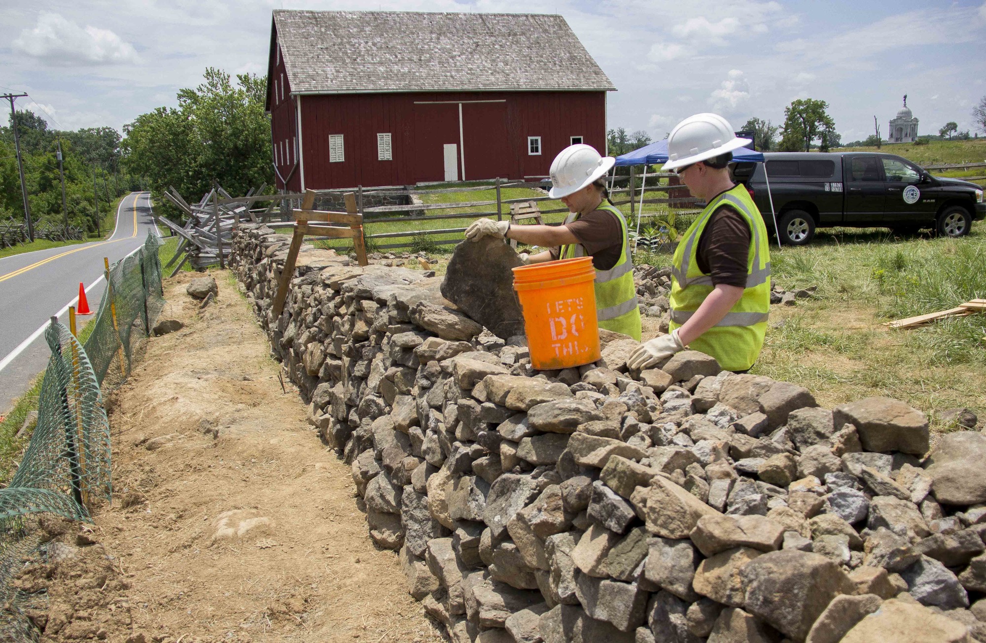 Two workers at a stone fence, one holding a large rock