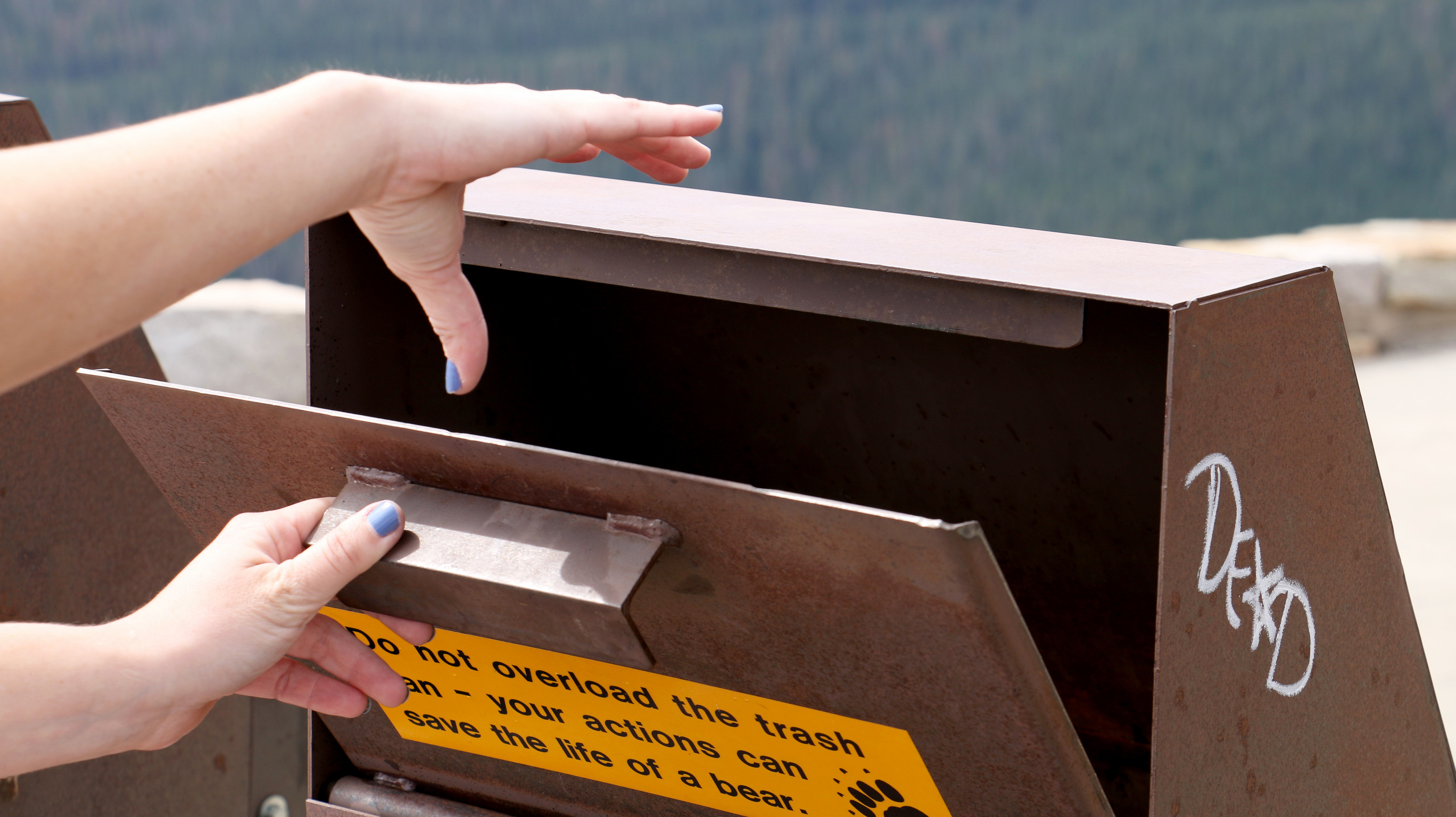 a person's hand throws a piece of trash into a brown metal container 