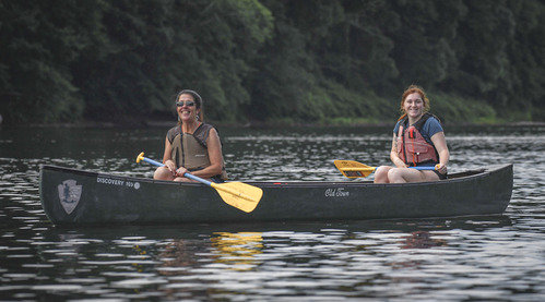 Two people sit in a canoe holding paddles on their lap.