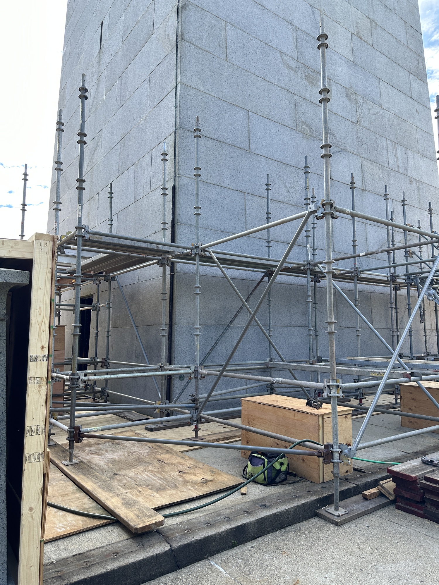 Scaffolding around the base of a granite monument, with plywood also being used. 