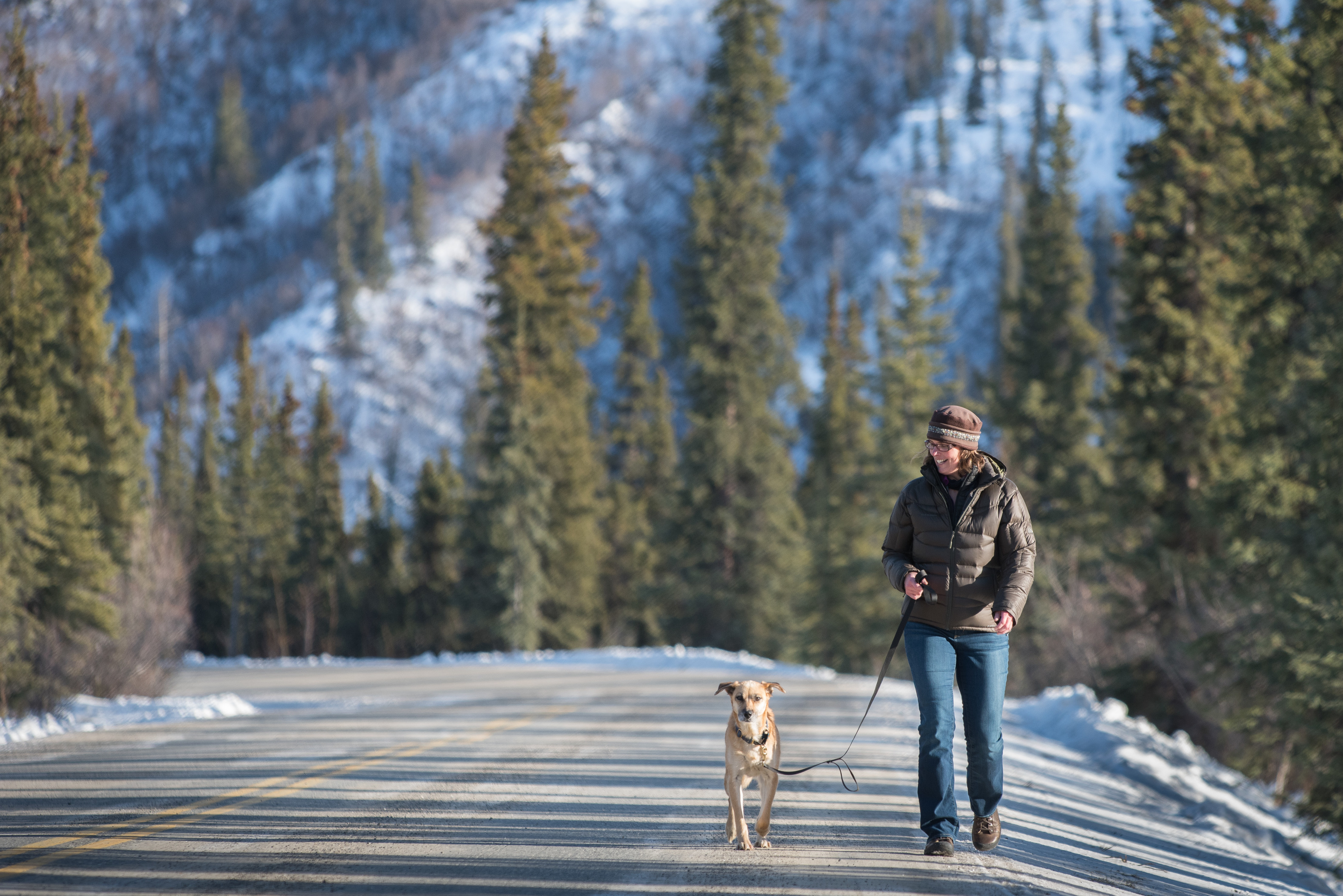a woman walking a dog on a road in a snowy forest