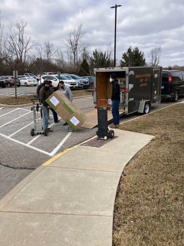 A man holding a hand truck loaded with three large boxes on a street.