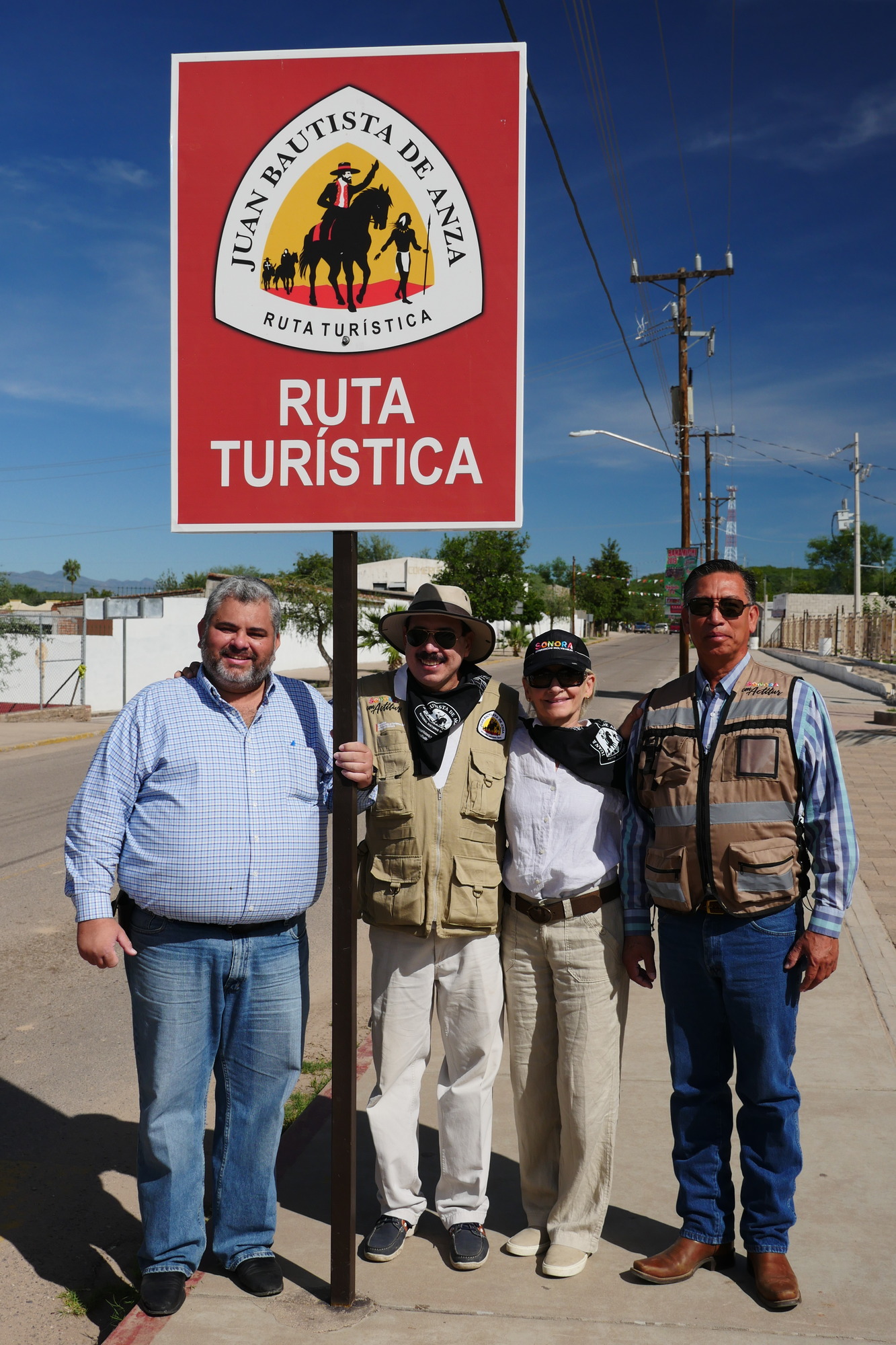 Four people smile next to an Anza Trail Ruta Turistica sign