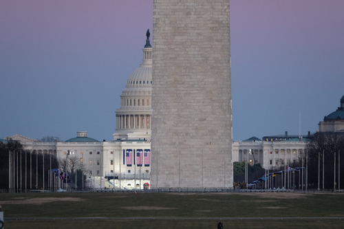 Washington Monument base in front of the U.S. Capitol building decorated with U.S. flags at dusk