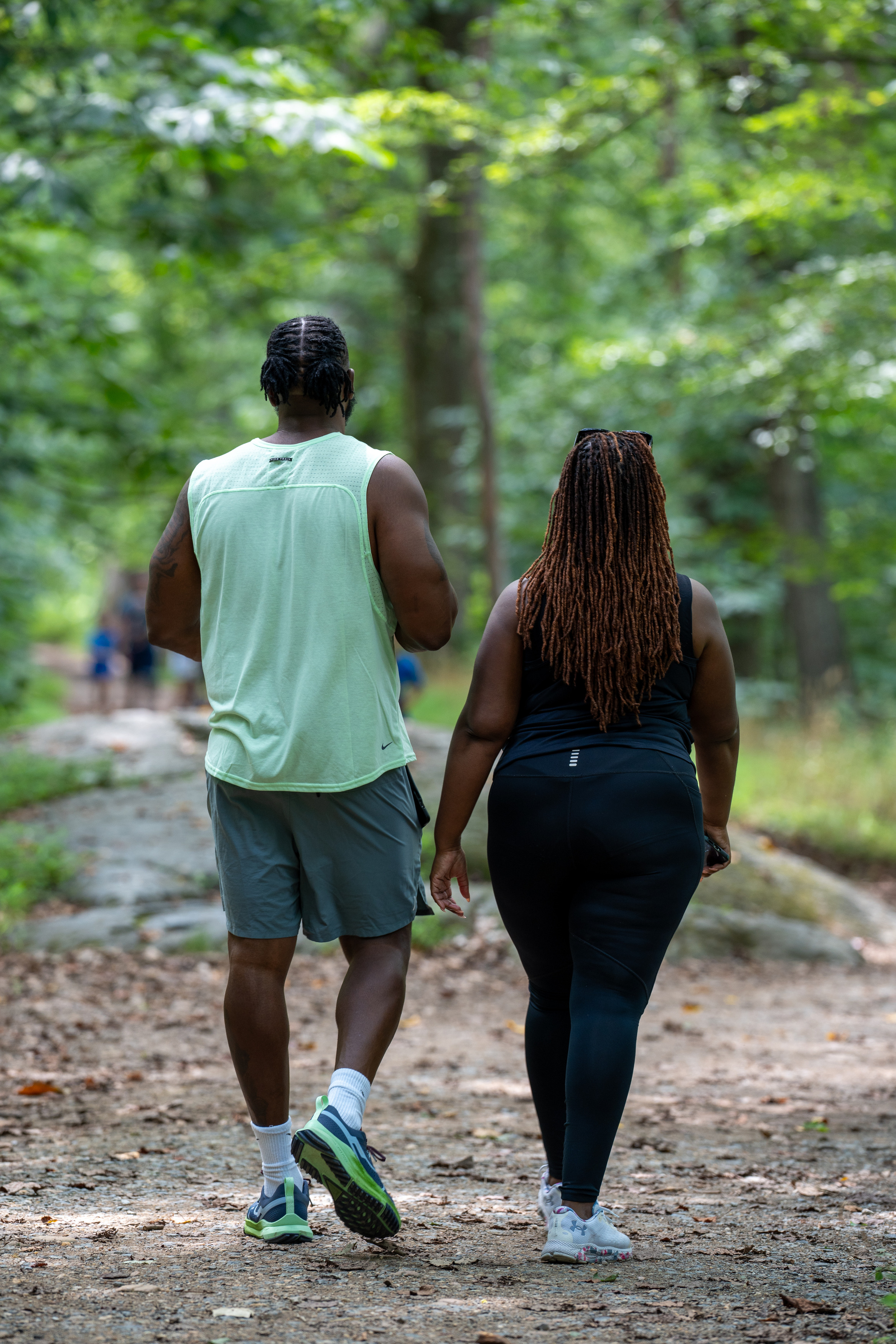 Two visitor walk away down a dirt trail in the forest.