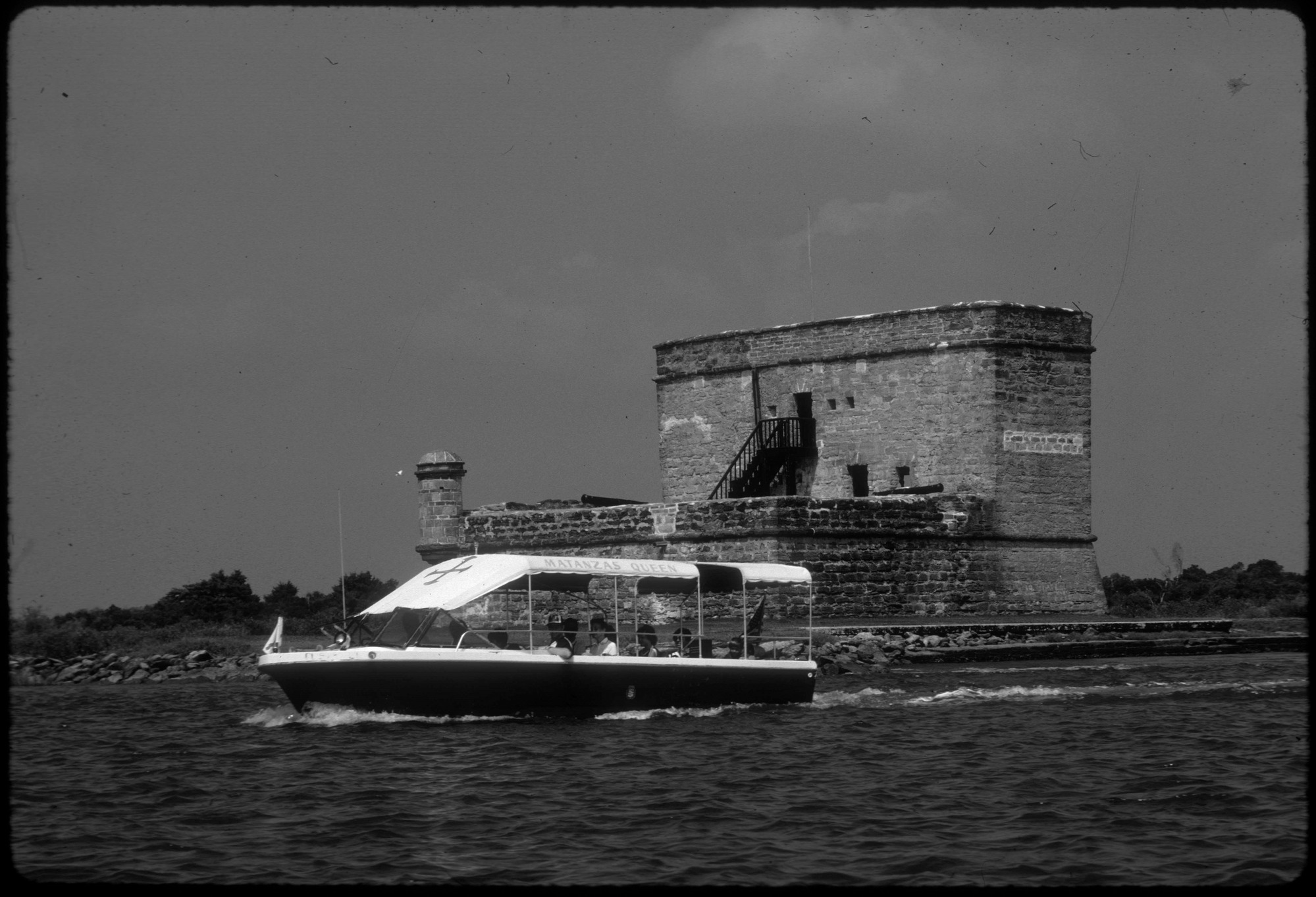 Dark v-hulled boat with white canopy. Fort in the background.