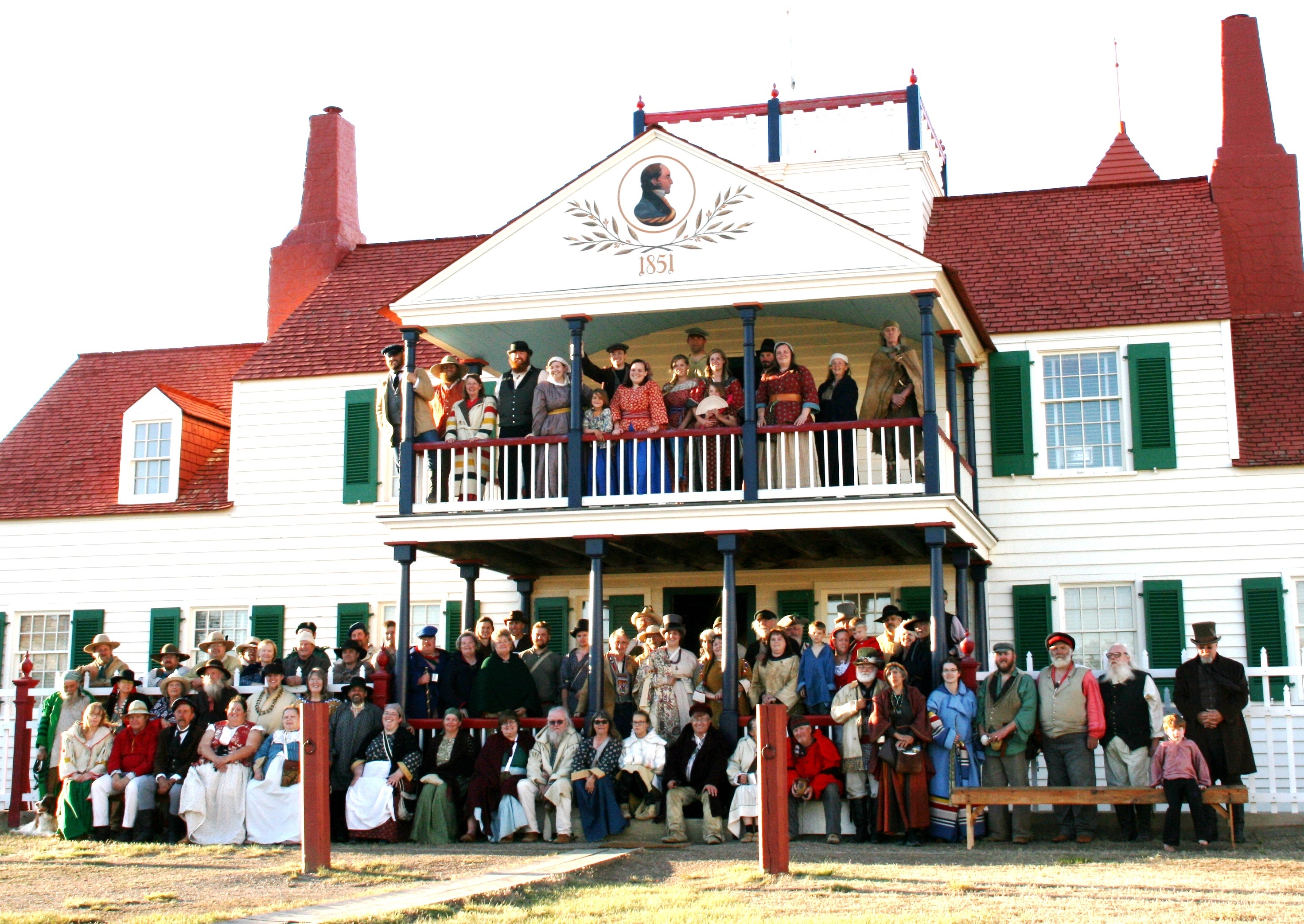 People in historic clothing pose in front of impressive home
