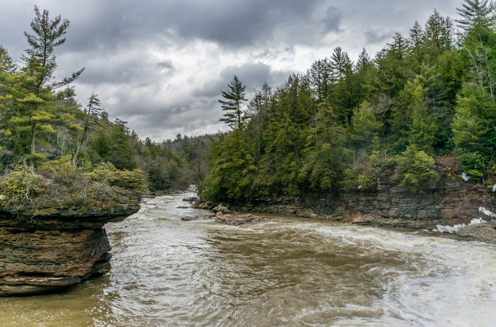 Storm clouds float over a river that has carved out a rocky tower in the middle of its path.