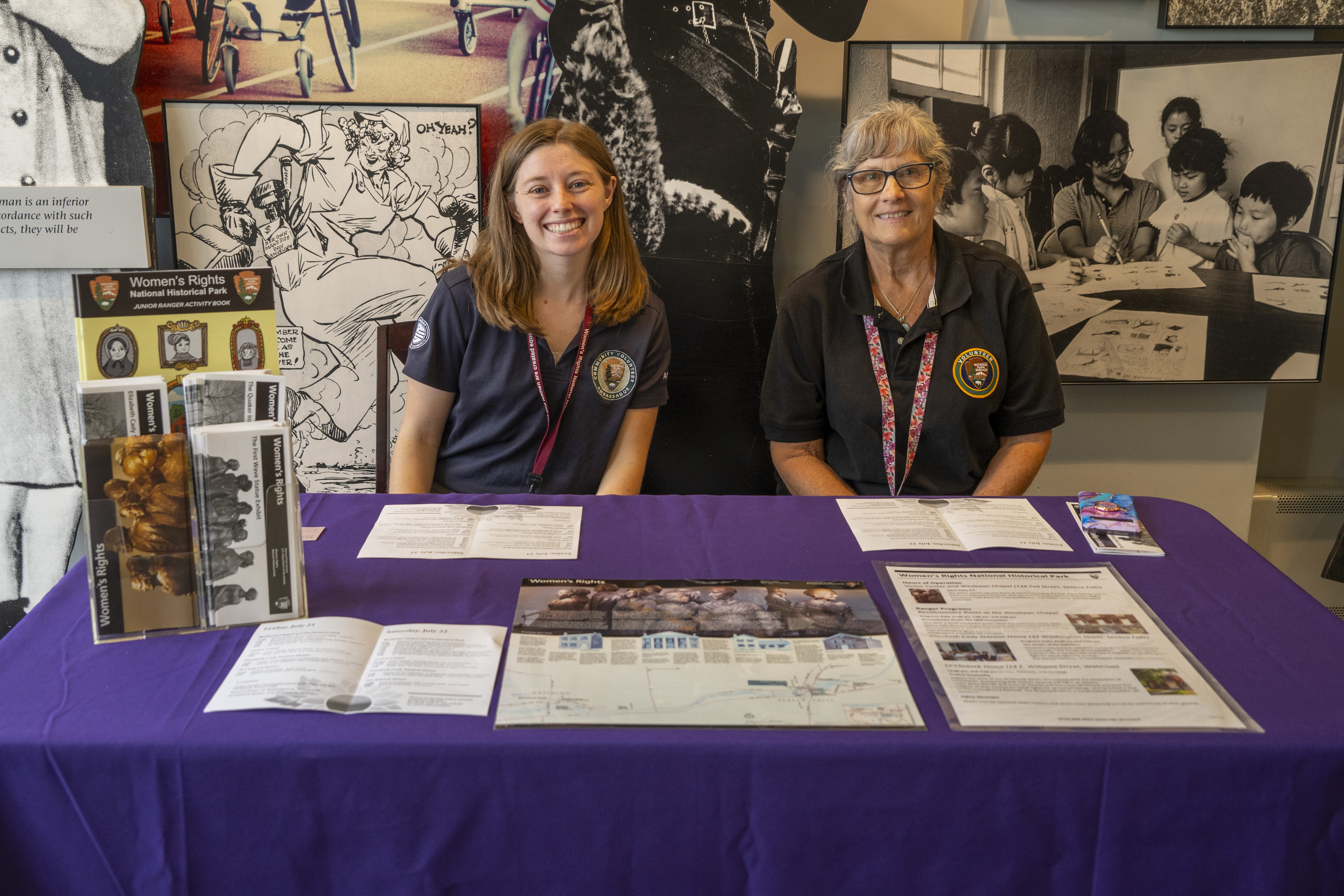 Two women sit at a table with brochures and maps.