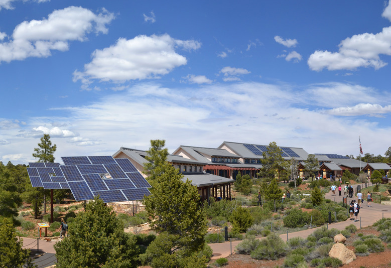 Grids of solar panels mounted on poles, with large building featuring panel-covered roof in background