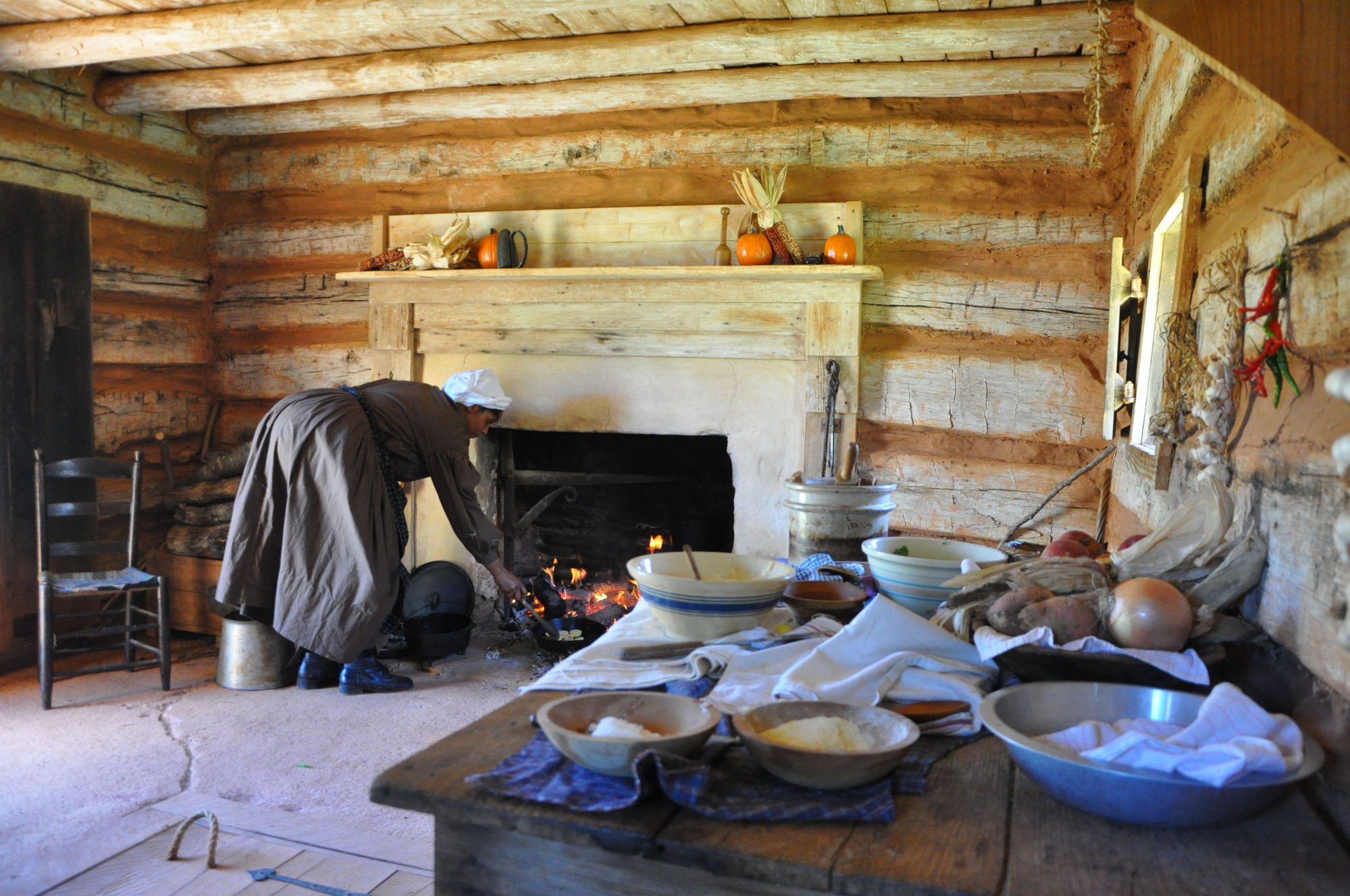 A woman in period clothing tends her fire in a log cabin