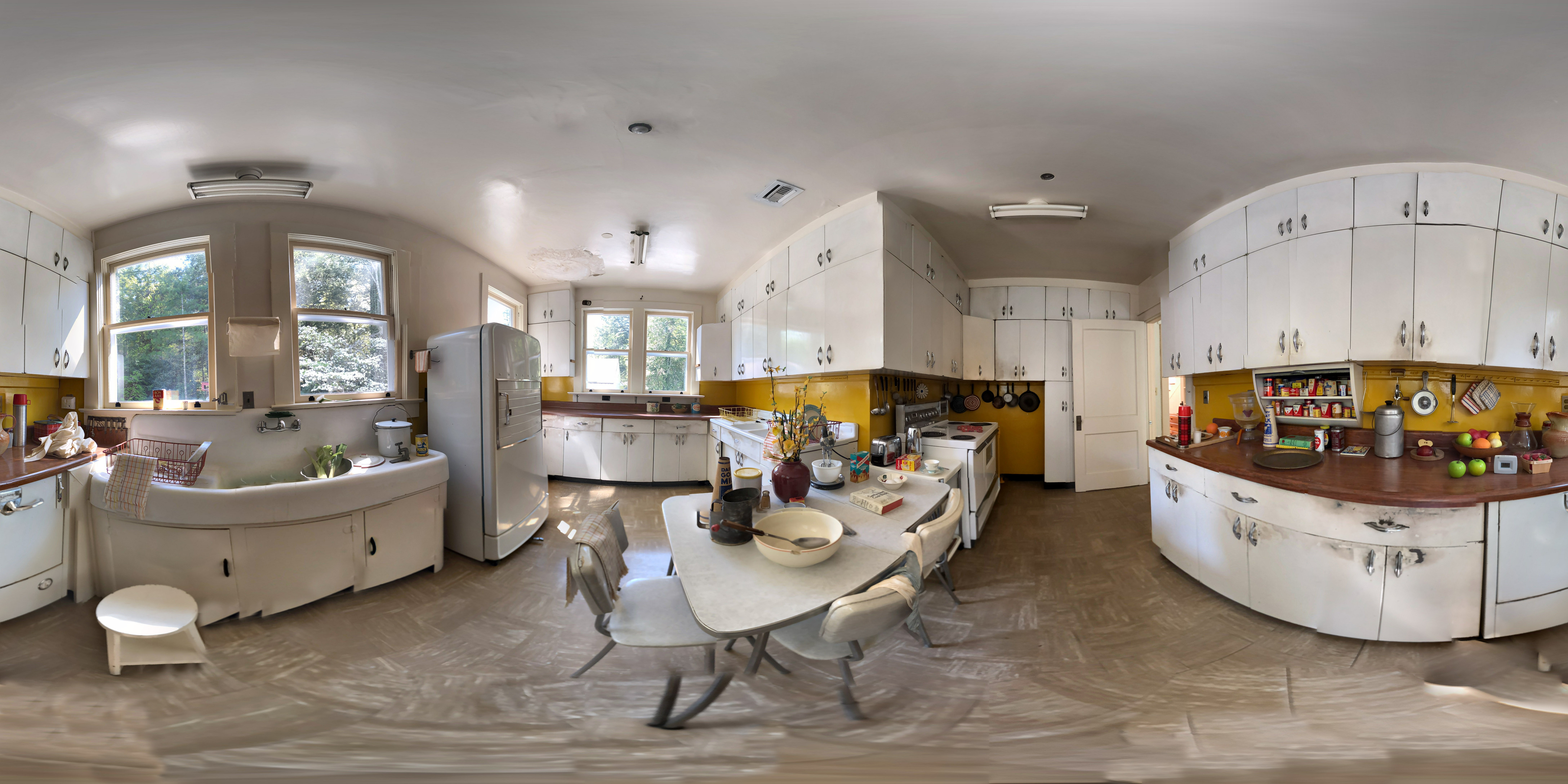 360 view of interior of a kitchen with white metal cabinets on three walls, a brown linoleum floor, white metal appliances and a table with bowls in the center.