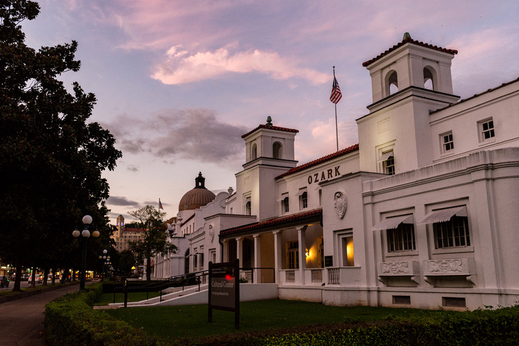 A white, hacienda style bathhouse takes on pink and purple hues as the sun sets. 