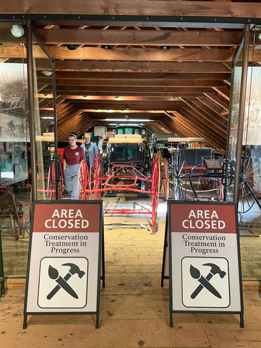Conservators and cultural resource staff leaving the carriage exhibit walking between “Area Closed Conservation Treatment in Progress” Signs 