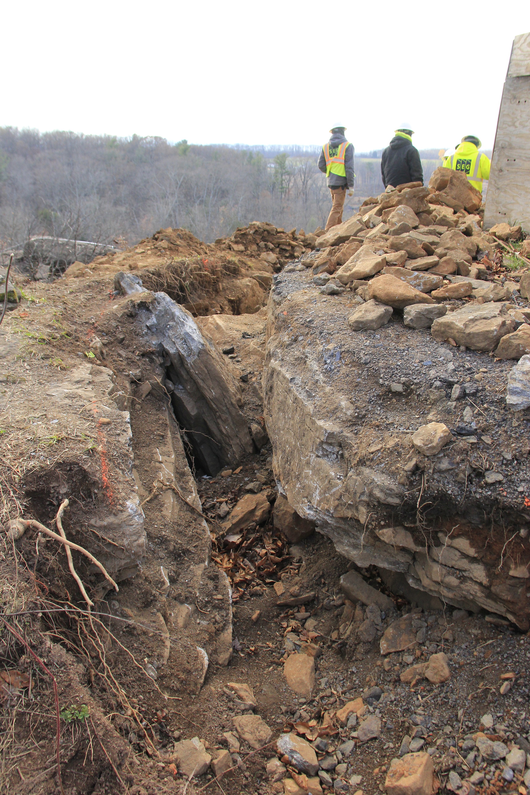 A large rift between two large boulders next to the 44th New York monument with construction workers in yellow jackets and vests just beyond them.