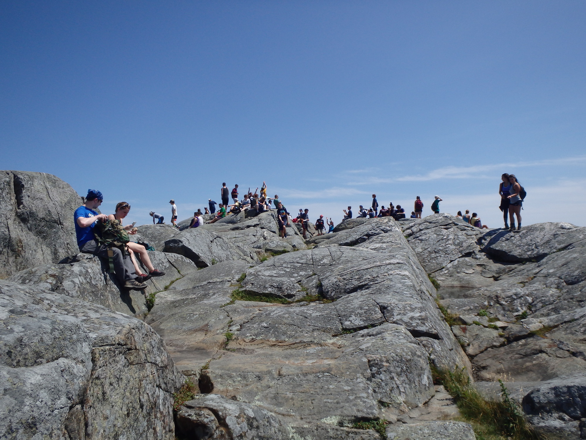 A  few dozen people atop a very steep rocky summit