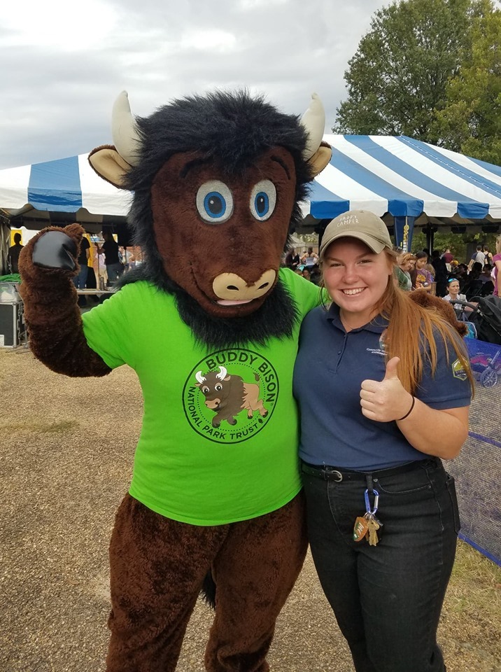 A person in a bison mascot costume stands beside a young intern. 