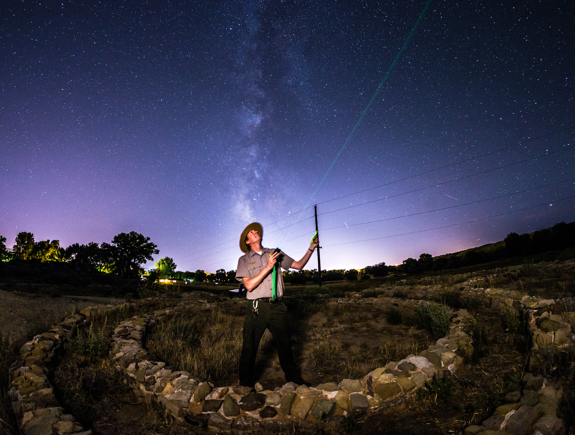 A park ranger stands inside an Ancestral Puebloan ring of stones and points his laser to a planet in the night sky at Aztec Ruins National Monument, New Mexico.
