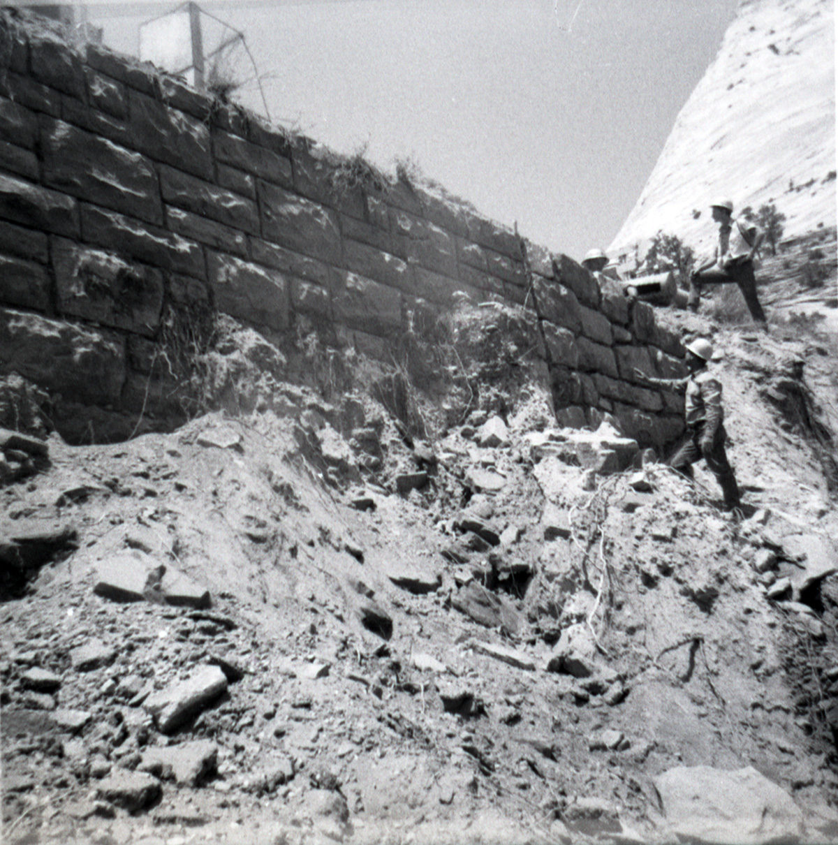 Men observing the repairs of retaining wall along East Rim road.