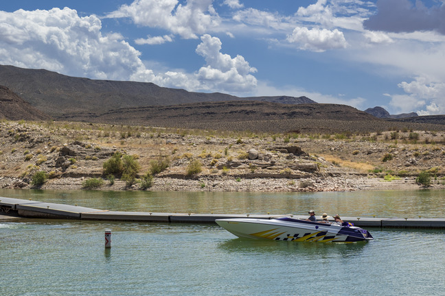 body of water surrounds boat dock with one boat,  cloudy sky and mountains in distance