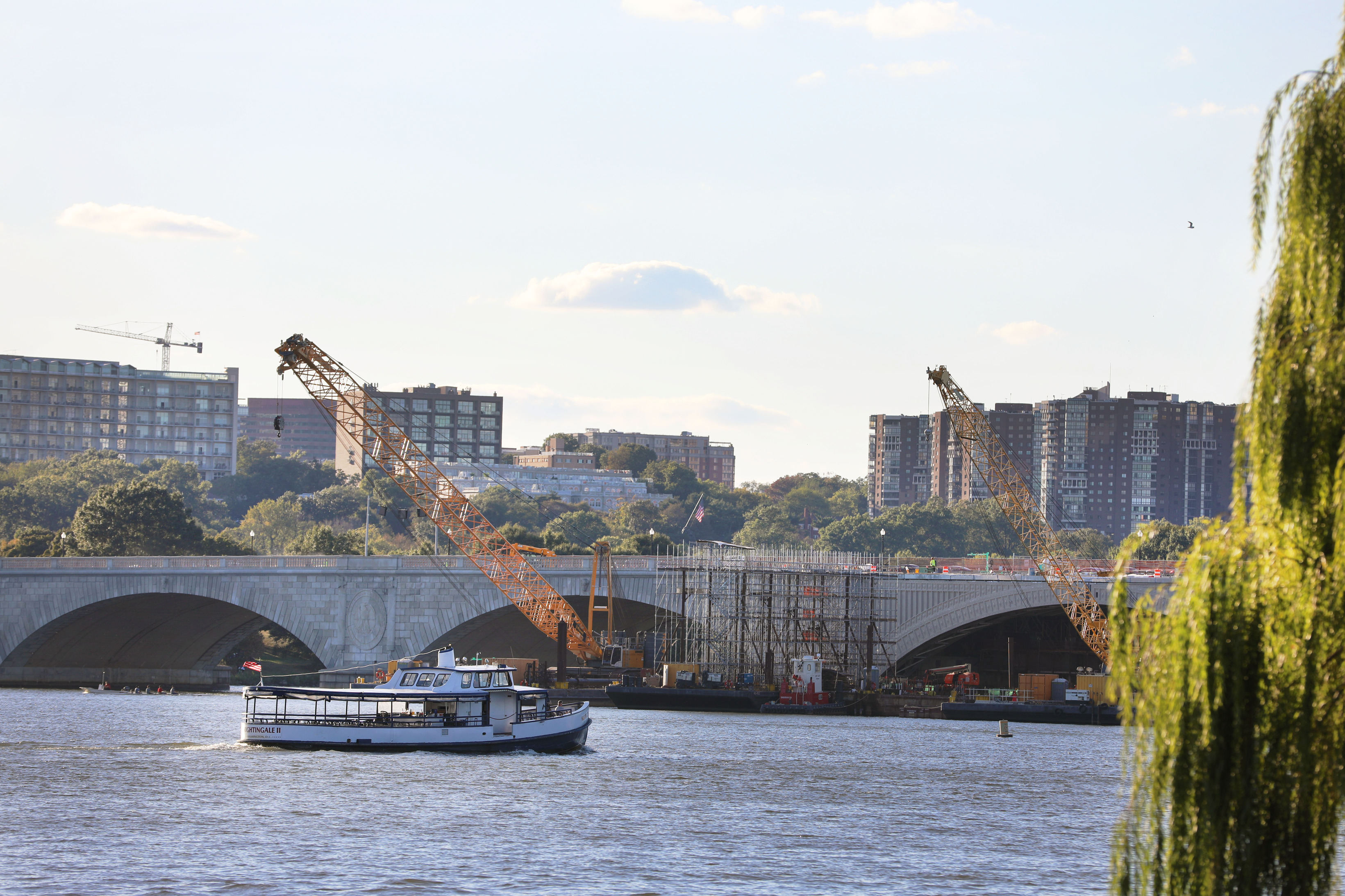 Construction on Arlington Memorial Bridge in October of 2019. Cranes on barges work on rehabilitating the bridge. A boat is in front of the bridge.  
