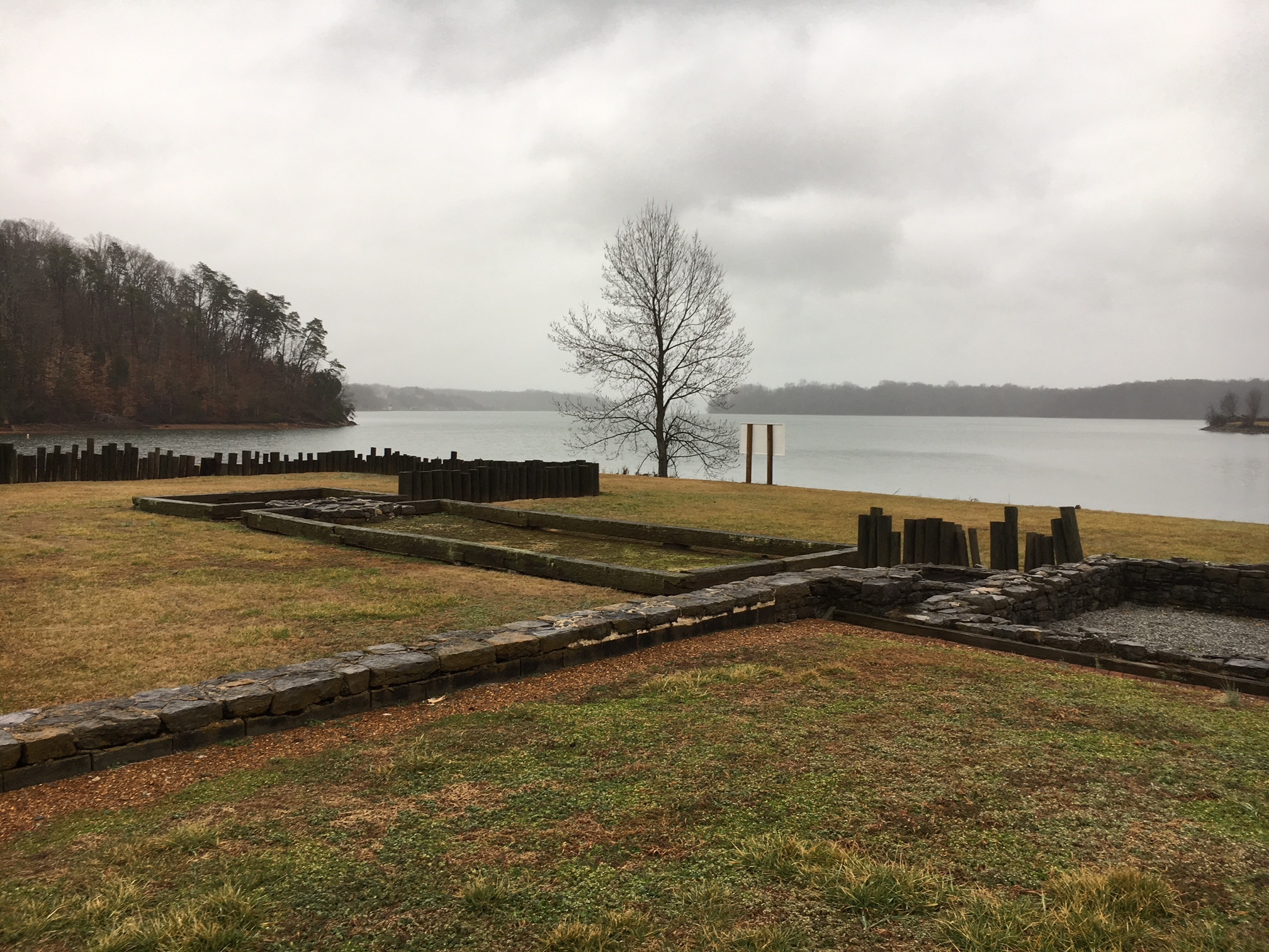 A grassland having stone wall in front of a lake.