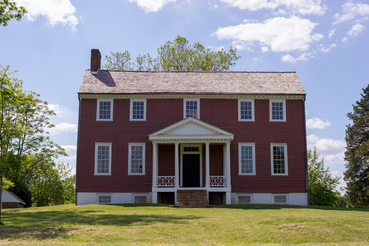 A two-story house with red siding and a small porch with columns at the front door.