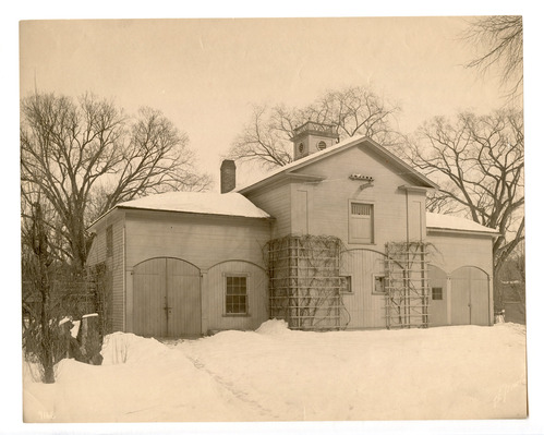 Black and white photograph of carriage house covered in snow.