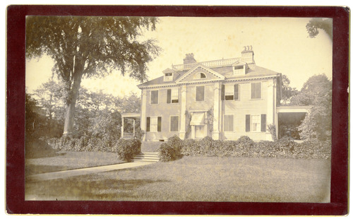Black and white photograph of Georgian mansion with heavy vegetation.