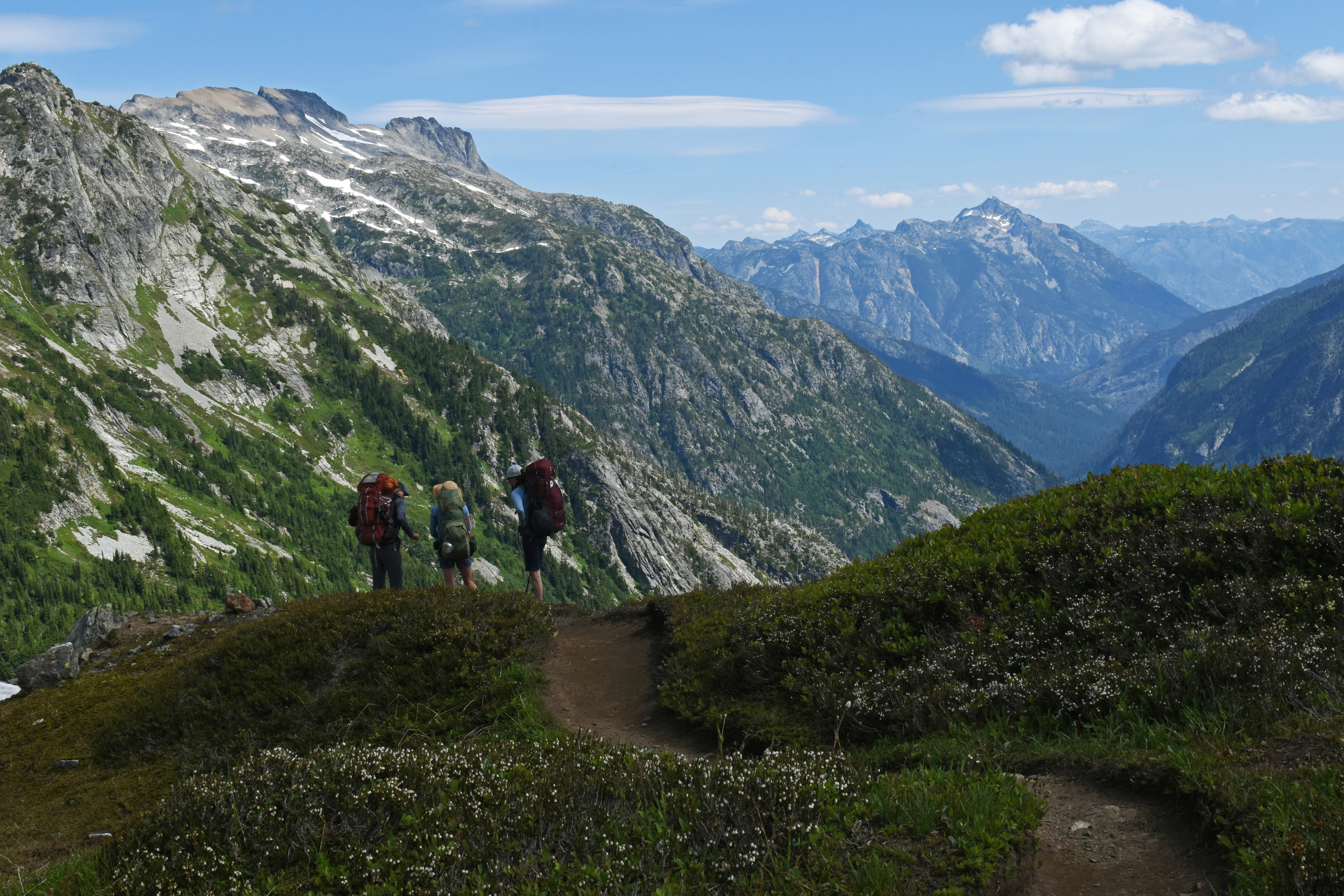 Three hikers take in the view of steep mountains and a deep green valley.