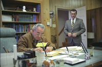 LBJ sits, leaning over desk, writing.