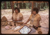 Two women stand in front of a display of Atsugewi crafts.