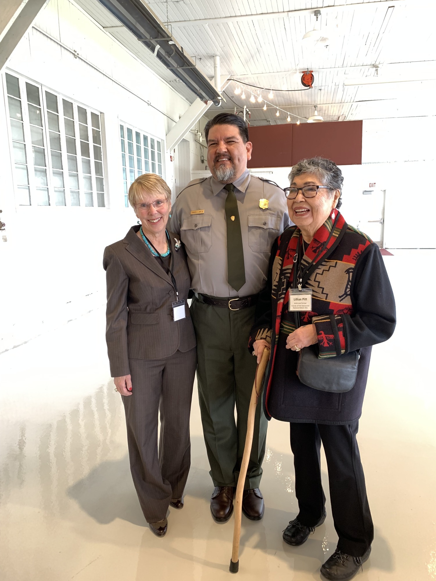 A man wearing a National Park Service uniform stands with a woman wearing a dark brown suit and a woman wearing a wool shawl.