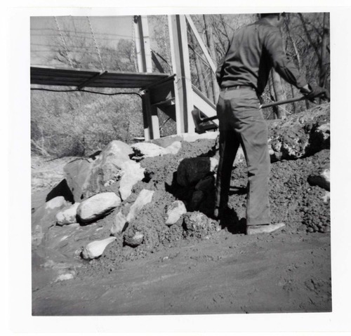 Man working on the protection/stabilization of the footings for the old Birch Creek suspension footbridge.