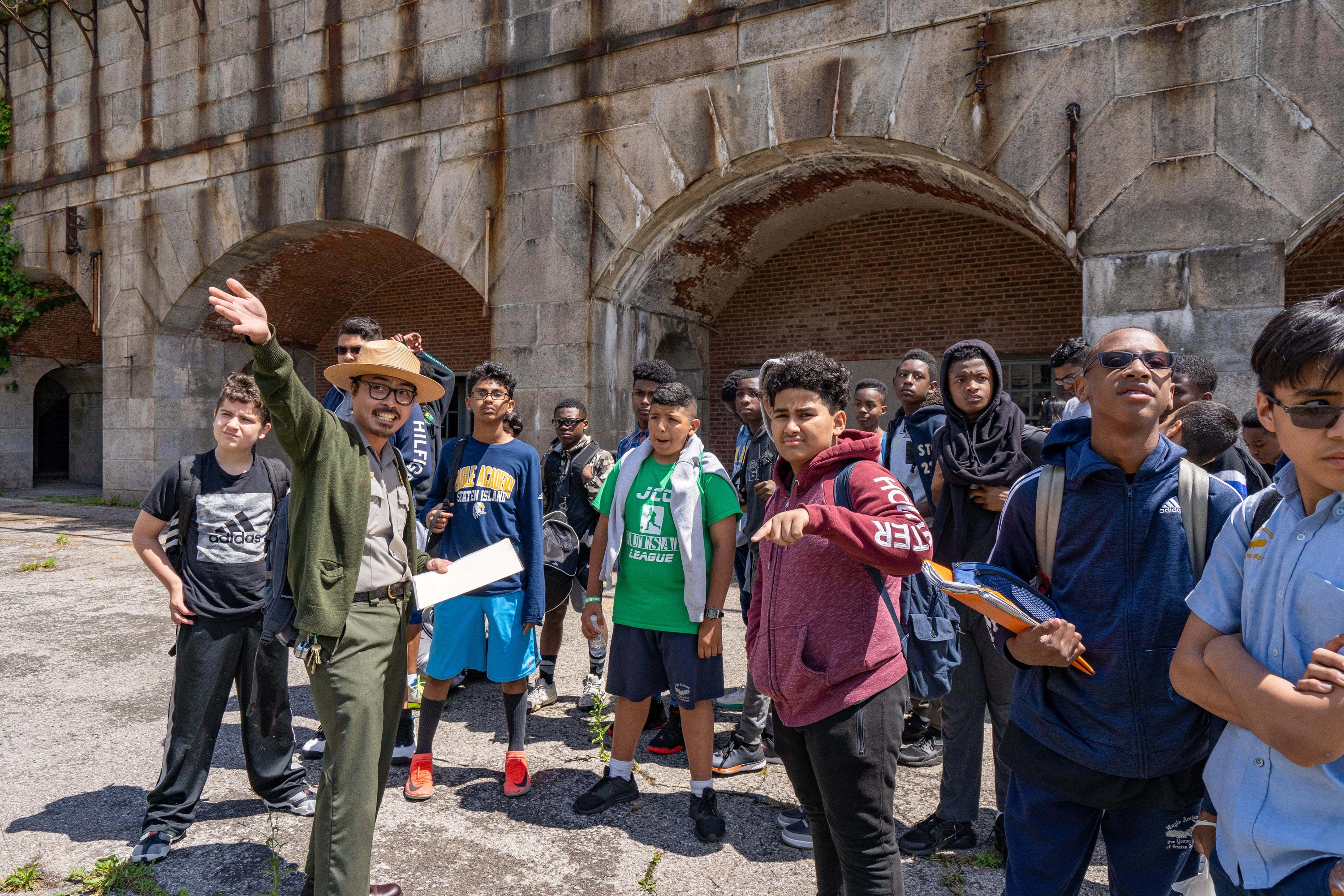 A park ranger gestures, while a class of teenage boys looks on.