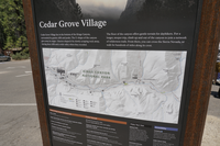 A metal panel with an image of a map on it. Sits in a metal frame. Behind it a large asphalt parking lot 