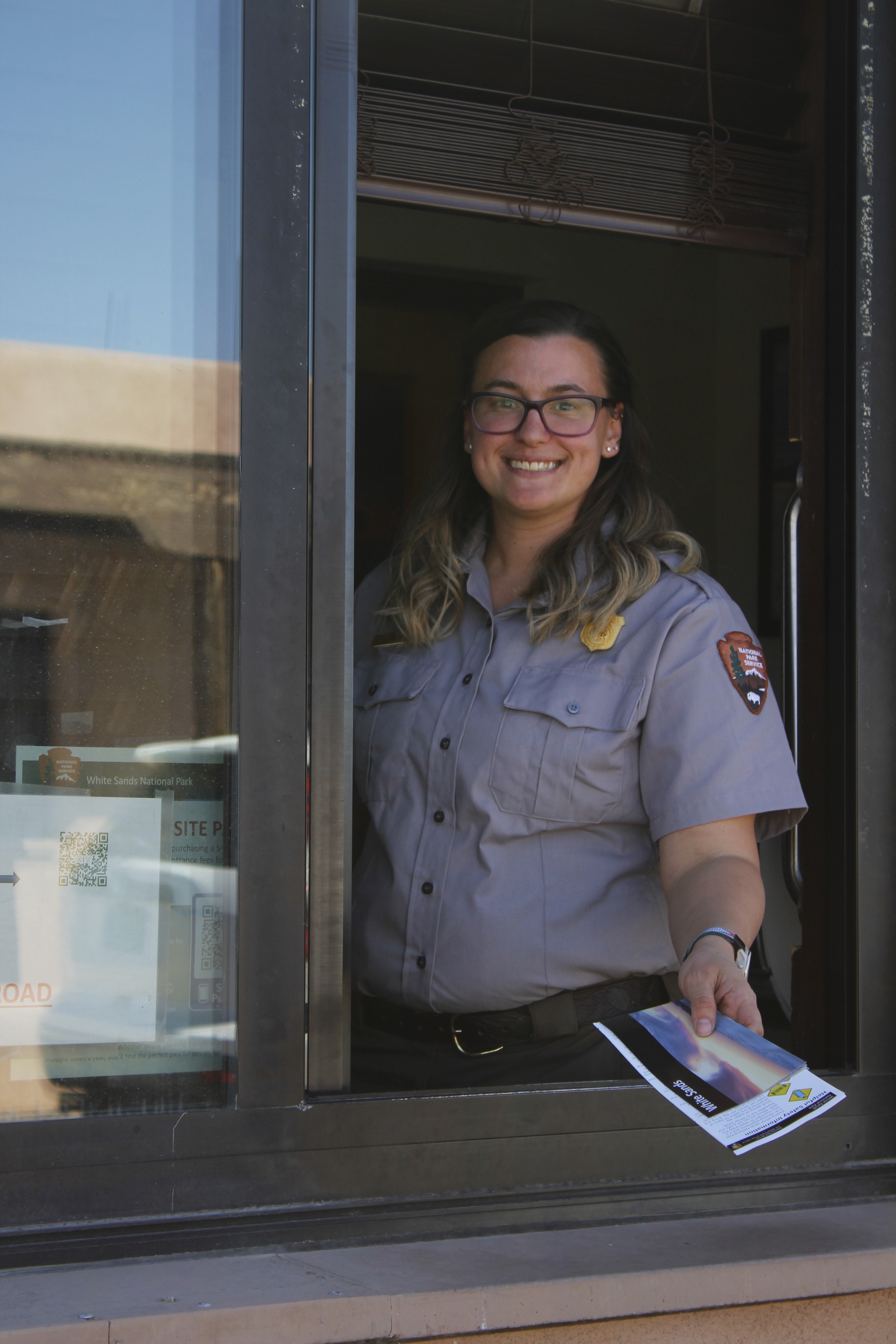 A woman in the park ranger uniform poses for a photo, framed by an open window. 
