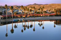 Sunrise with palm trees and motel reflected in still water - mountains in background