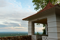 White, stucco gazebo with a pointy, red tile roof overlooks an expansive landscape at sunset.