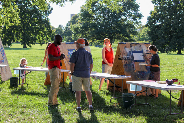 Visitors interacting with paint materials and talking with program leader.