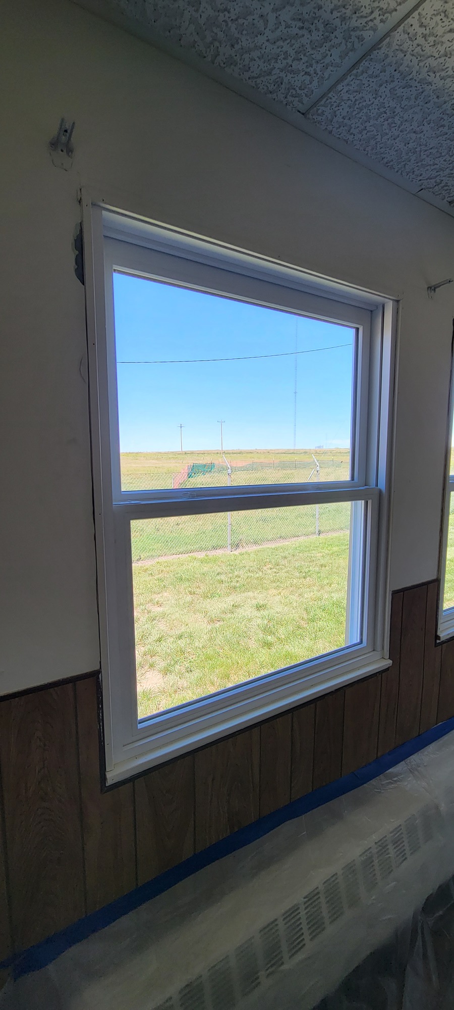 Through a white wall wood paneling, a view through a window of a grassy field.